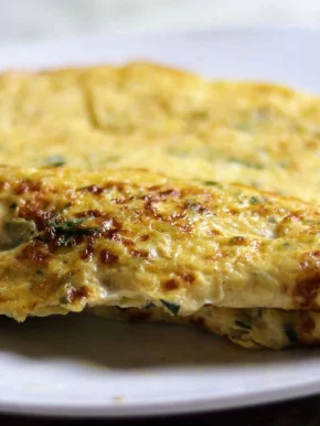 A freshly made, fluffy Indian omelette sits folded in half on a plate